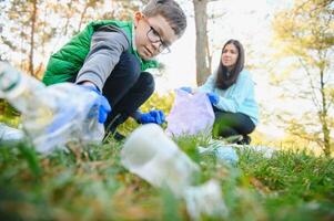 lächelnd Junge pflücken oben Müll im das Park mit seine Mutter. Freiwillige Konzept. foto