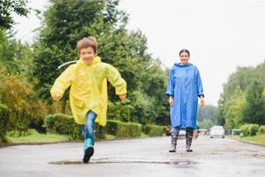 Mutter und Kind, Junge, spielen im das Regen, tragen Stiefel und Regenmäntel foto