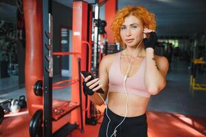 lächelnd charmant jung Frau Athlet im Kopfhörer mit Smartphone und Hören zu Musik- im Fitnessstudio foto