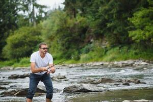 bärtig Mann fangen Fisch. Sommer- Freizeit. reifen Mann Angeln auf das Teich. Porträt von heiter Senior Mann Angeln. männlich Angeln. Fischmann gehäkelt rotieren in das Fluss warten groß Fisch foto