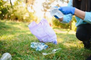 Damen Hände im rot Gummi Handschuhe. Frau sammelt Müll im das Tasche. Freiwillige spülen Müll im das Sommer- Park. nett progressiv Frau Herstellung ein Anstrengung zu Hilfe das Umgebung foto