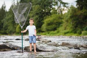 süß Junge im Weiß t Hemd Angeln im das Fluss und hat Spaß, lächelt. Ferien mit Kinder, Feiertage, aktiv Wochenenden Konzept foto