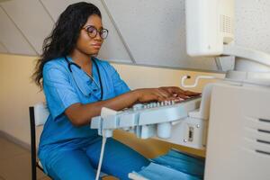 lächelnd afrikanisch Frau Arzt mit Ultraschall Scanner im Hand, Arbeiten auf modern Ultraschall Scannen Maschine im Licht Zimmer im Klinik. Porträt von 4d Ultraschall Scannen Maschine Operator foto