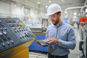 Ingenieur im Helm ist mit ein Laptop im ein schwer Industrie Fabrik foto