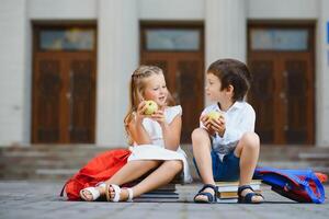 glücklich Kinder - - Junge und Mädchen mit Bücher und Rucksäcke auf das zuerst Schule Tag. aufgeregt zu Sein zurück zu Schule nach Urlaub. voll Länge draussen Porträt. foto