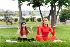 Mutter und Tochter tun Yoga Übungen auf Gras im das Park beim das Tag Zeit foto