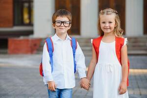 glücklich Kinder gehen zurück zu Schule. Schüler von primär Schule gehen Studie mit Rucksack draußen. Kinder gehen Hand im Hand. Anfang von Unterricht. zuerst Tag von fallen. Junge und Mädchen von elementar Student. foto