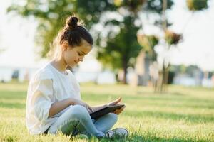 wenig Mädchen Sitzung auf Gras und spielen Tablette PC, Tonen Foto. foto