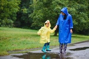 Mutter und Kind, Junge, spielen im das Regen, tragen Stiefel und Regenmäntel foto