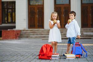 glücklich Kinder - - Junge und Mädchen mit Bücher und Rucksäcke auf das zuerst Schule Tag. aufgeregt zu Sein zurück zu Schule nach Urlaub. voll Länge draussen Porträt. foto