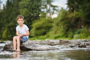 süß Junge im Weiß t Hemd Angeln im das Fluss und hat Spaß, lächelt. Ferien mit Kinder, Feiertage, aktiv Wochenenden Konzept foto