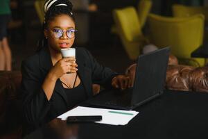 konzentriert weiblich Büro Arbeiter mit Computer im Kaffee Geschäft. afrikanisch amerikanisch Geschäft Frau Arbeiten auf Laptop im Cafe und suchen weg. Internet Technologie Konzept foto