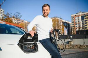 Mann Gebühren ein elektrisch Auto beim das Laden Bahnhof foto