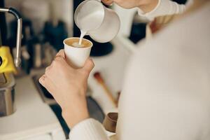 schließen oben von weiblich Barista macht Kaffee und gießt es in ein Becher während Arbeiten im Kaffee Geschäft foto