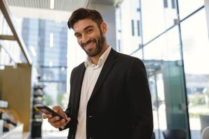 Geschäftsmann halten Handy, Mobiltelefon Telefon und suchen beim Kamera mit Lächeln Stehen auf Büro Hintergrund foto