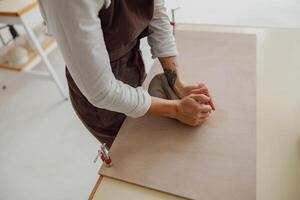 schließen oben von weiblich Töpfer im Schürze knetet Stück von Lehm mit ihr Hände auf Tabelle im Studio foto