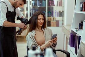 Schönheit Salon weiblich Kunde mit ihr Telefon während Friseur tun ihr Haar foto