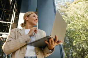 Unterseite Aussicht von Frau Unternehmer Arbeiten auf Laptop draußen auf modern Gebäude Hintergrund foto