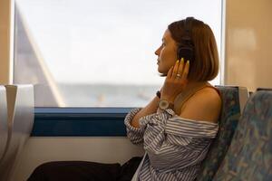 Frau im Kopfhörer während Reisen im Öffentlichkeit Transport und suchen Aussicht draußen das Fenster foto