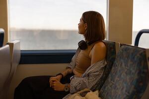 Frau im Kopfhörer während Reisen im Öffentlichkeit Transport und suchen Aussicht draußen das Fenster foto