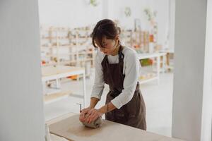 ziemlich Frau vorbereiten Lehm zu erstellen ein Becher auf ein hölzern Tabelle im Keramik Studio foto