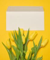 Briefumschlag und Strauß von Blühen Gelb Tulpen mit Grün Blätter auf ein Gelb Hintergrund foto