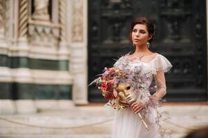 das Mädchen-Braut ist mit schön Blume Muster wie ein Maske im Florenz, stilvoll Braut im ein Hochzeit Kleid Stehen mit ein Maske im das alt Stadt, Dorf von Florenz. Modell- Mädchen im Florenz foto
