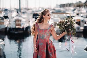 jung Modell- Mädchen im ein schön Kleid mit ein Strauß von Blumen auf das Strand im Frankreich. Mädchen mit Blumen im Frühling Provence auf das Französisch Riviera foto