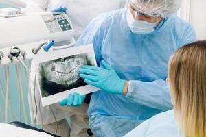 das Zahnarzt zeigt an das Einzelheiten von das Röntgen zu seine geduldig im das Arzt Büro foto