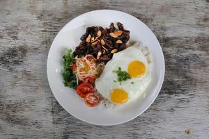 uns Rindfleisch tapas mit sonnig Ei und Reis mit Tomate serviert im Gericht isoliert auf hölzern Hintergrund oben Aussicht von Frühstück foto