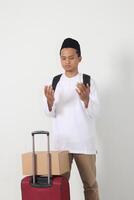 Porträt von attraktiv asiatisch Muslim Mann Tragen Koffer, erziehen Hände, beten Vor Verlassen. gehen Zuhause zum eid Mubarak. isoliert Bild auf Weiß Hintergrund foto