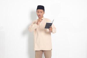 Porträt von aufgeregt Muslim Mann im koko Hemd mit peci Schreiben auf seine Notizbuch. glücklich asiatisch Kerl nehmen Anmerkungen. isoliert Bild auf Weiß Hintergrund foto