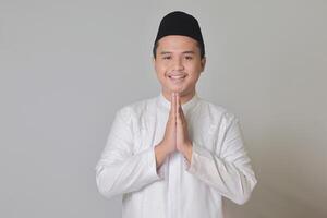Porträt von asiatisch Muslim Mann im Weiß koko Hemd zeigen entschuldigen und herzlich willkommen Hand Geste. isoliert Bild auf grau Hintergrund foto