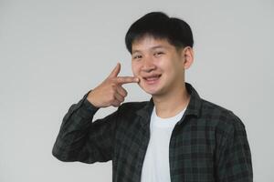 glücklich asiatisch Teen Junge zeigen beim Zahnspange. lächelnd asiatisch Teenager Mann zeigen beim seine Dental Hosenträger auf ein Licht grau Hintergrund. Porträt gut aussehend Mann im Studio Konzept. foto