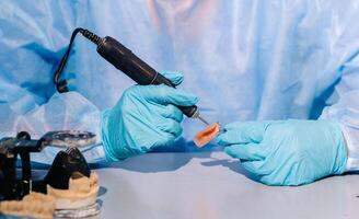 ein maskiert und behandschuhte Dental Techniker funktioniert auf ein Prothese Zahn im seine Labor foto