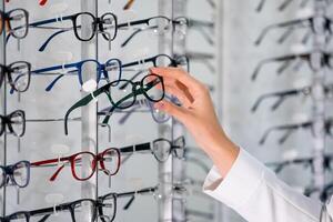 Reihe von Brille beim ein Optiker. Brille Geschäft. Stand mit Brille im das Geschäft von Optik. Frau Hand wählt Brille foto