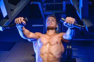 mit nacktem Oberkörper jung Bodybuilder tun Bank Drücken Sie zum Brust. stark Abs. Blau Licht Filter. Foto von das Seite.