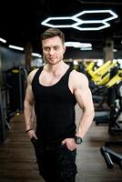 zuversichtlich muskulös Trainer auf das Fitnessstudio. Mann mit sportlich Körper Stehen im das Fitnessstudio. foto