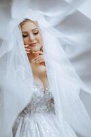 schön jung Braut halten Schleier im Weiß Hochzeit Kleid, Porträt von blond Braut im Hotel Zimmer, Morgen Vor Hochzeit. foto