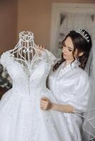 Braut berühren ihr Hochzeit Kleid. hoch Qualität Foto. ein schön jung Braut im ein Weiß Petticoat ist Stehen durch das Bett, berühren ihr Hochzeit Kleid. foto