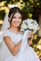 Porträt. ein Brünette Braut im ein Kleid und ein Schleier, mit ein schick Krone, posiert mit ein Strauß. Silber Schmuck. schön bilden und Haar. Herbst Hochzeit. Feier foto