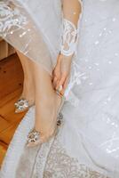 jung Braut im schön Hochzeit Kleid Putten auf Schuhe drinnen. Braut Kleider Schuhe Vor das Hochzeit Zeremonie. Detail von Braut Putten auf hoch hochhackig Sandale Hochzeit Schuhe. Hochzeit Braut Schuhe. foto