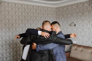 ein jung Bräutigam und seine komisch freunde Pose zum das Kamera. ein Gruppe von jung Menschen Umarmung das Bräutigam und fröhlich gratulieren ihn. glücklich Freunde. freunde im das Zimmer. Hochzeit Tag. foto