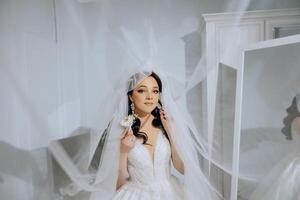 schön jung Braut halten Schleier im Weiß Hochzeit Kleid, Porträt von Brünette Braut im Hotel Zimmer, Morgen Vor Hochzeit. foto