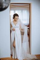 in voller Länge Porträt von ein unglaublich schön Braut im ein Dressing Kleid im ein Schlafzimmer im das Morgen. Vorbereitung von das Braut zum das Hochzeit. foto