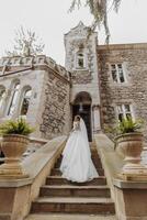 zurück Aussicht von Braut im Weiß elegant Kleid Gehen im alt Schloss draußen. das Braut klettert das Stufen, ein Kleid mit ein lange Zug foto