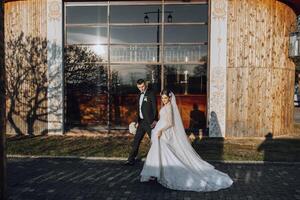 ein Hochzeit Paar ist Gehen im Natur auf ein Herbst Tag. glücklich jung Braut und elegant Bräutigam halten Hände. ein stilvoll Paar von Jungvermählten auf ihr Hochzeit Tag. foto