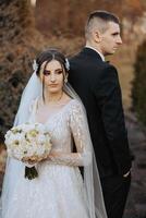 Porträt von ein lächelnd Braut mit ein Strauß von Blumen umarmen ihr Mann während suchen beim das Kamera. schön Hochzeit Feier. Hochzeit Frisur mit ein Schleier. Paar im Liebe. foto