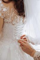 das jung Braut ist Stehen von das zurück. ein schön Frau im ein Hochzeit Kleid, im ein Zimmer in der Nähe von ein Fenster. attraktiv Mädchen im ein Weiß Hochzeit Kleid mit ein lange Zug foto