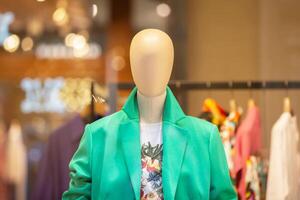 ein weiblich Mannequin im ein Grün Jacke hinter das Glas von ein Geschäft Fenster. foto